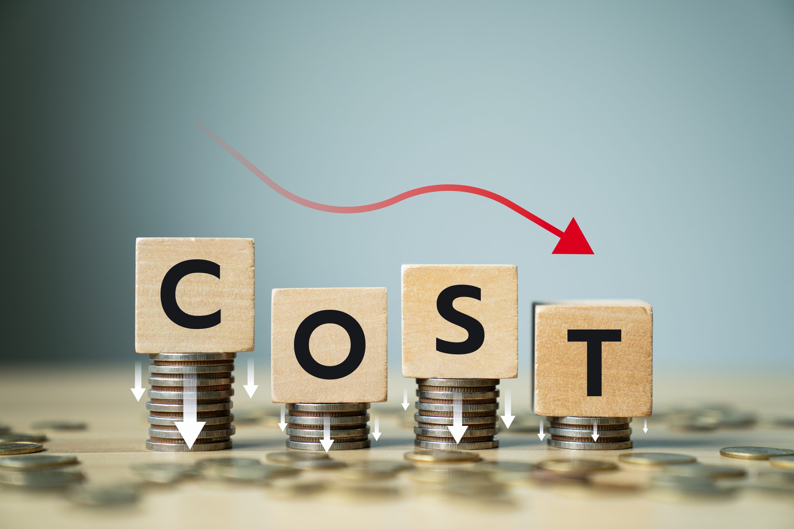 Concept of cost reduction in business finance with wooden blocks spelling COST placed on descending stacks of coins, red downward arrow, symbolizing decreasing expenses, saving strategy, efficiency
